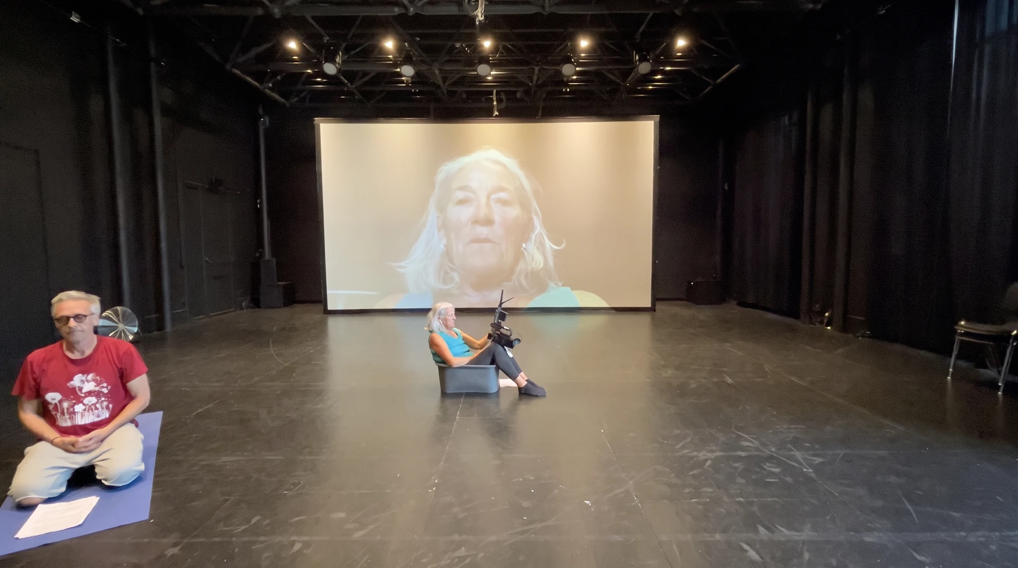 Une interprète assise tient une caméra devant son visage projeté en grand format au Grütli.
